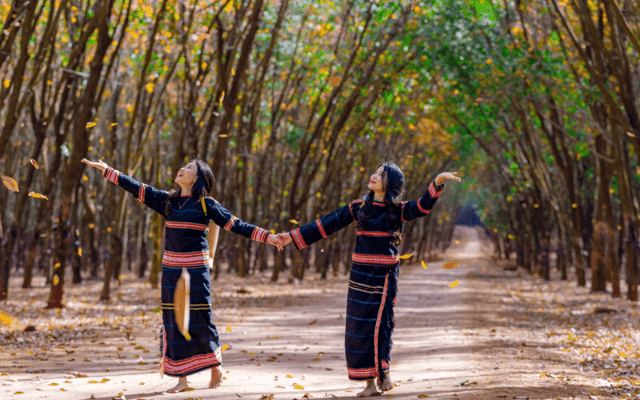两位身着埃德族（&Ecirc; Đ&ecirc;）服饰的少女，正在捕捉橡胶叶飘落的瞬间