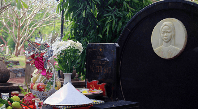 The grave of female martyr Võ Thị Sáu at Hàng Dương Cemetery, Côn Đảo, always adorned with offerings of conical hats and 'le-ki-ma' (canistel) fruit, a specialty from her hometown of Đất Đỏ.