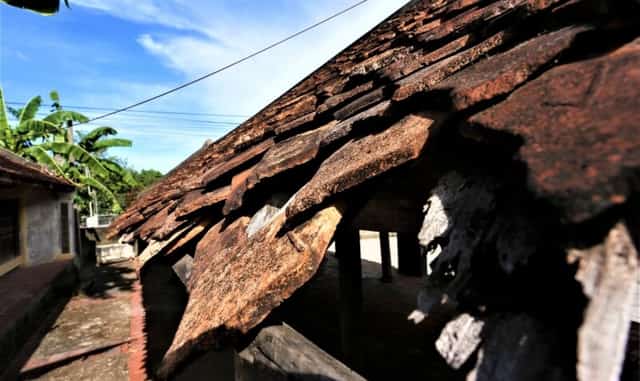The fish-scale tiles on the communal house roof are falling off and showing signs of damage over time.